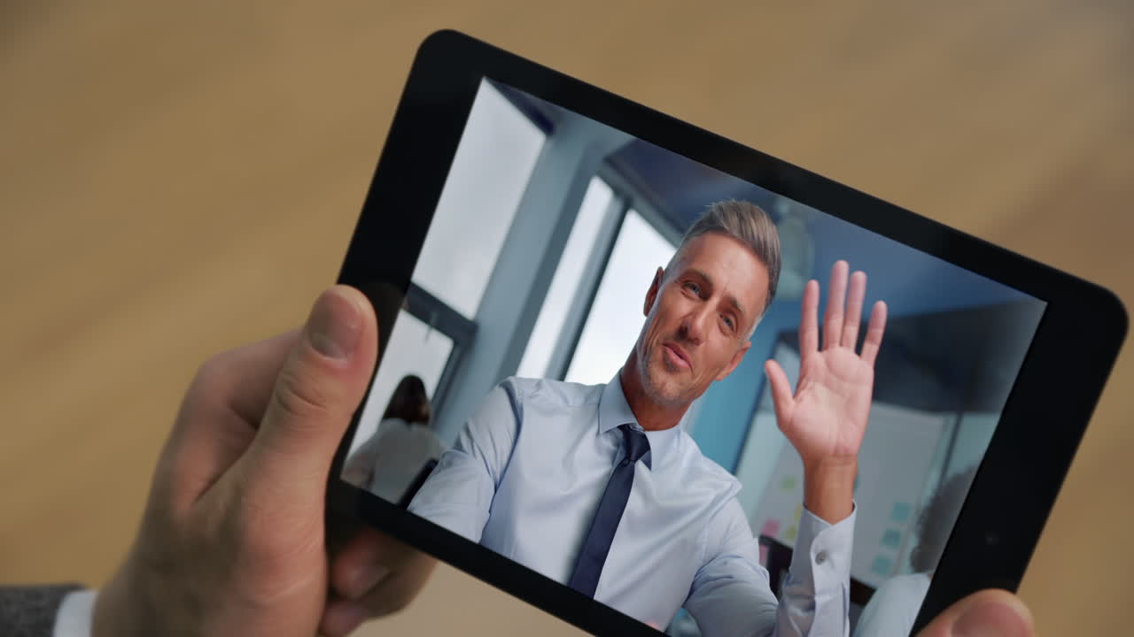 Forretningsmand taler på tablet under onlinemøde med uigenkendelig mand, nærbillede af rum