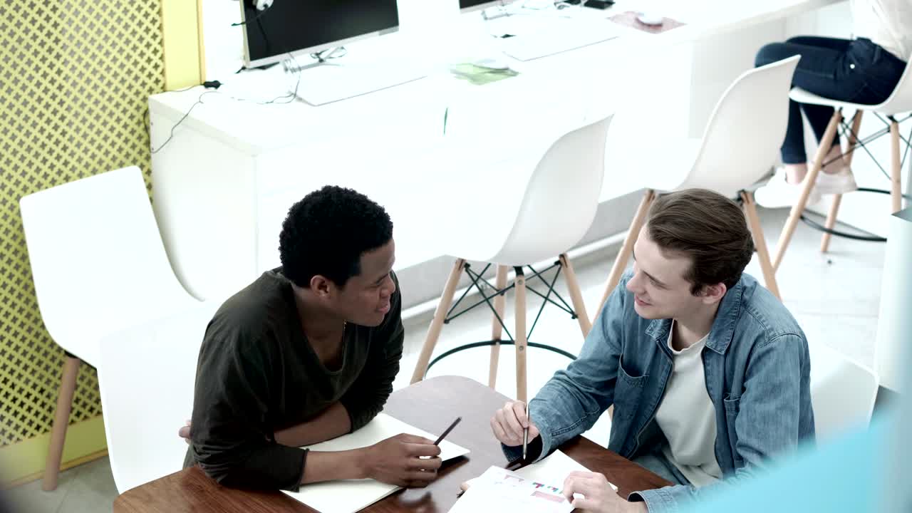 dos estudiantes universitarios sentados en un escritorio y discutiendo la investigación en la sala de trabajo