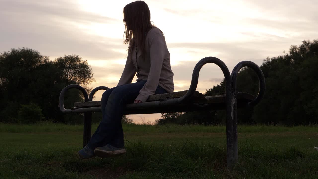 mujer solitaria sentada en un banco de parque de madera al atardecer