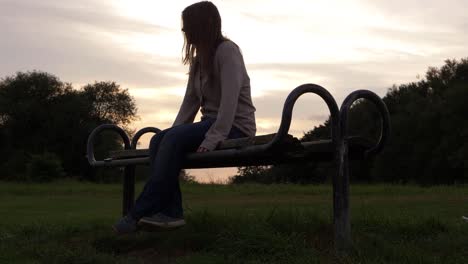 mujer solitaria sentada en un banco de parque de madera al atardecer