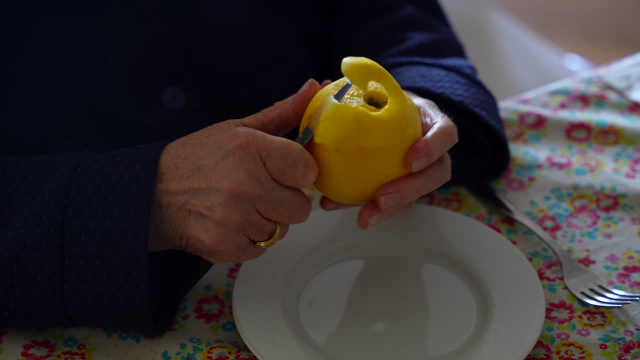 Manos envejecidas pelan meticulosamente una manzana con movimientos circulares usando un cuchillo, mostrando precisión