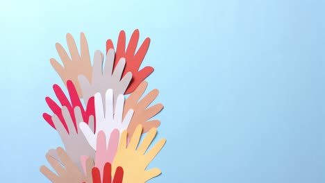 close up of hands together made of colourful paper on blue background with copy space