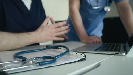 two unrecognizable  male caucasian doctors discussing over laptop in the background and stethoscope in the foreground