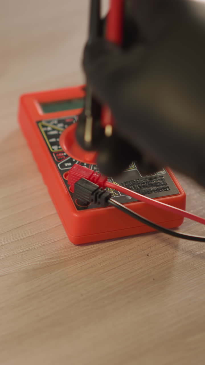 una vista de cerca de un técnico en una bata de laboratorio blanca y guantes de mano negros ajustando el voltímetro, con otras herramientas en la mesa
