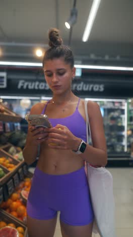 young woman shopping for fruits and using smartphone in a supermarket