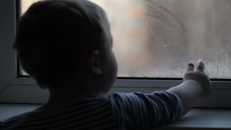 Little-boy-watching-through-the-misted-window