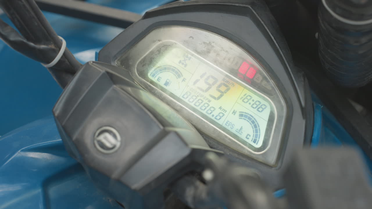 Closeup atv dashboard digital speedometer display backlit blue plastic housing, ignition lights flickering, odometer readout visible, textured lens with dirt and grime, startup numbers changing