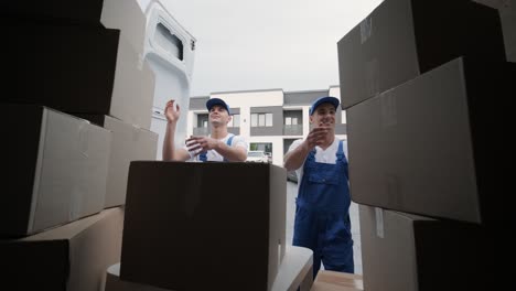 two young workers of removal company unload boxes and furniture from minibus into customer's home