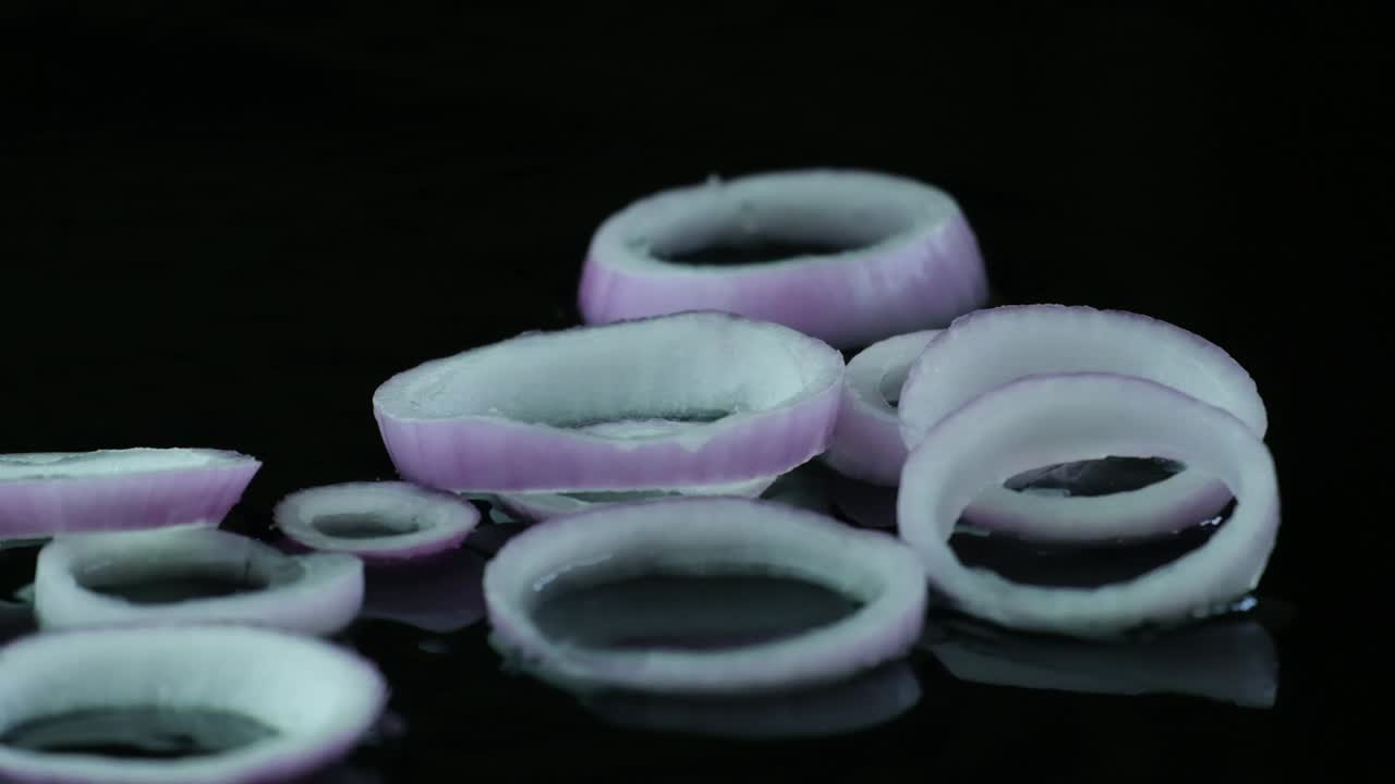 흑색 반사 표면 에 느리게 던져지는 양파 조각 의 영화적 영상, 슬로모