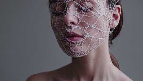 young woman wearing delicate white net veil over closed eyes, creating enigmatic atmosphere with soft, ethereal beauty and contemplative expression against minimalist background