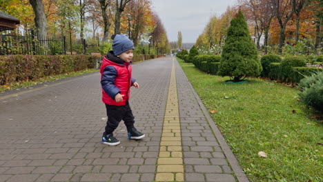 cute lovely boy in cap and jacket is in the park. active toddler jumping happily and smiling.