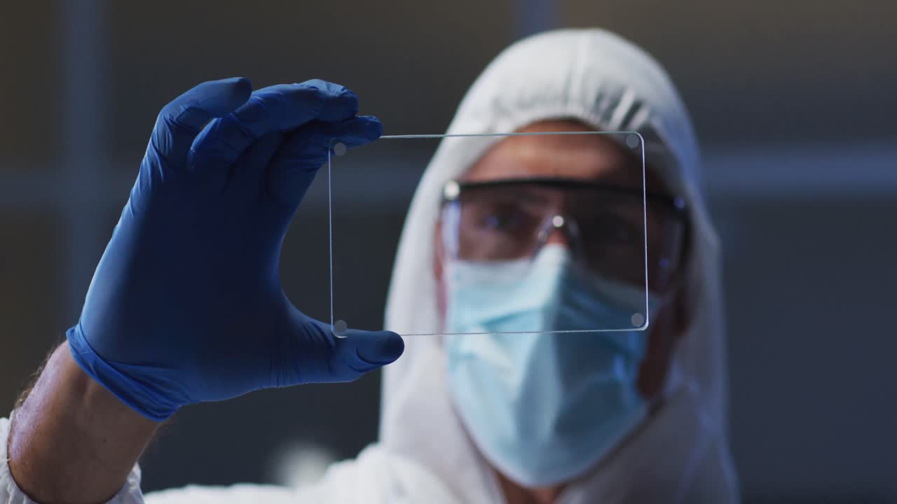 Caucasian male medical worker wearing protective clothing and gloves using handheld interface in lab