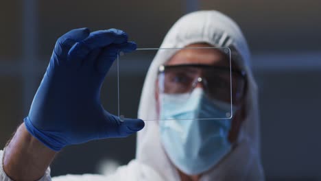 caucasian male medical worker wearing protective clothing and gloves using handheld interface in lab