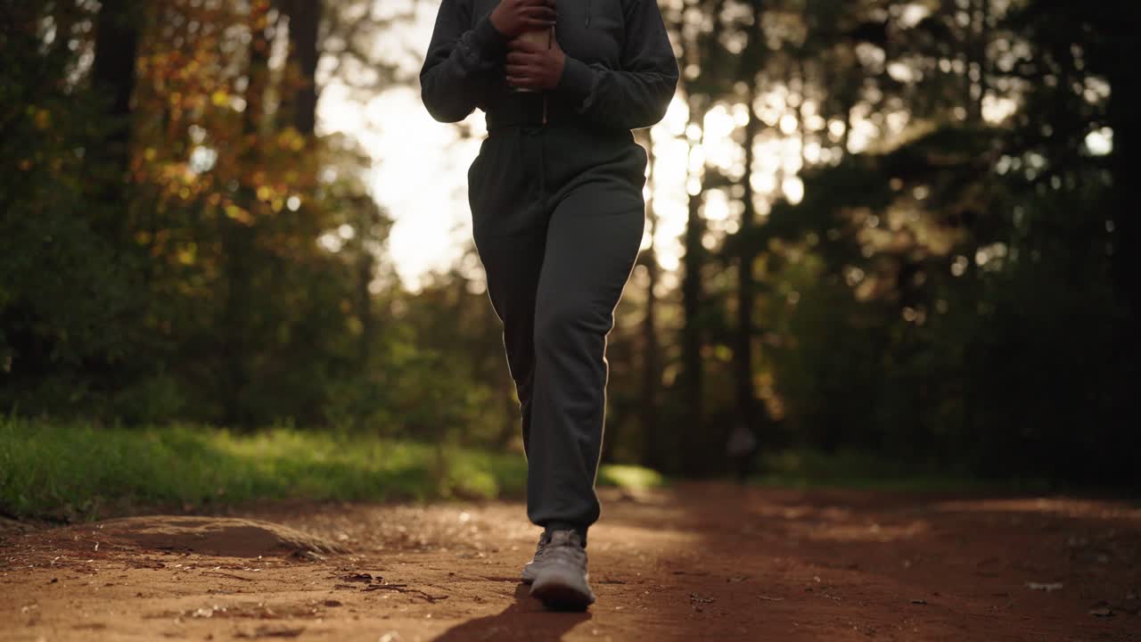 Una mujer caminando sola por una ruta de senderismo a través de un hermoso bosque mientras el sol sale entre los altos árboles