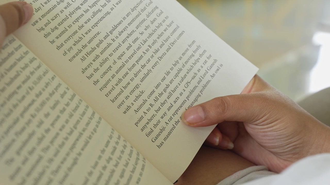 Close-up of a woman's hand gently pressing and smoothing an open book page while reading, with clearly visible printed text and soft natural window light illuminating.