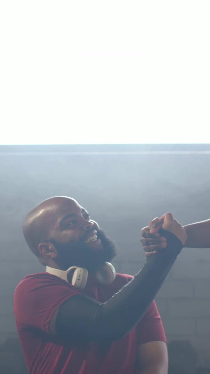 Video vertical: Hombre sonriente con camiseta roja y auriculares, con la mano extendida, entrando por la derecha debajo de un panel, saludando.
