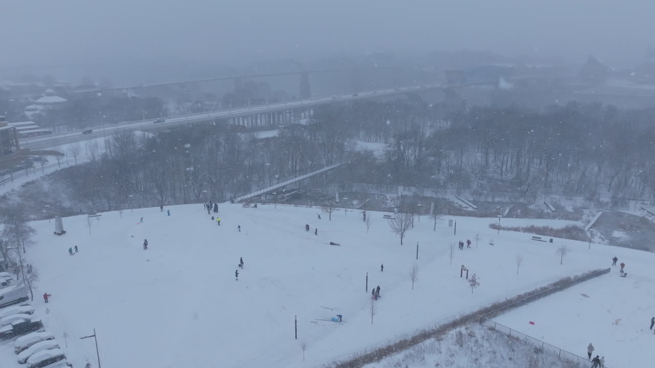 Aerial footage flying away from a small hill with people sledding on it in Renaissance Park in Chattanooga, TN during a snowstorm.