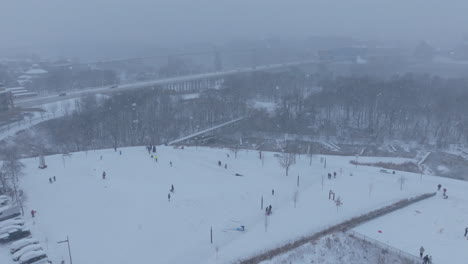 aerial footage flying away from a small hill with people sledding on it in renaissance park in chattanooga, tn during a snowstorm.