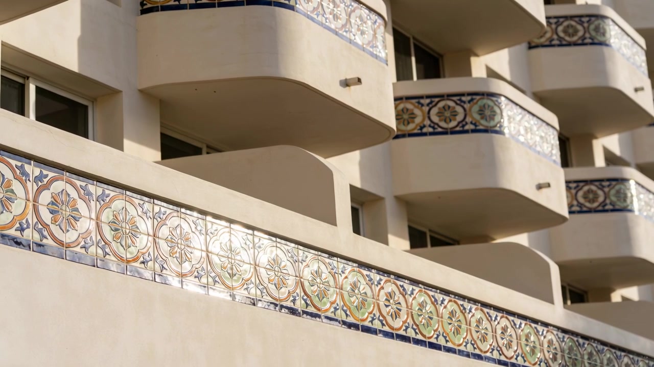 Luz solar em movimento e a câmera se aproximando revelando uma faixa de azulejos, destacando varandas curvas na fachada.