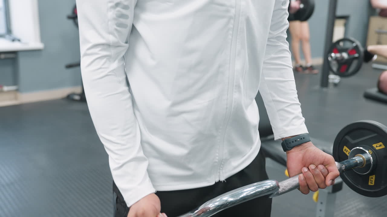 Close up of person lifting chrome barbell on rubber floor with gym members visible in background, focused grip, muscle engagement, workout action, equipment details in modern fitness setting