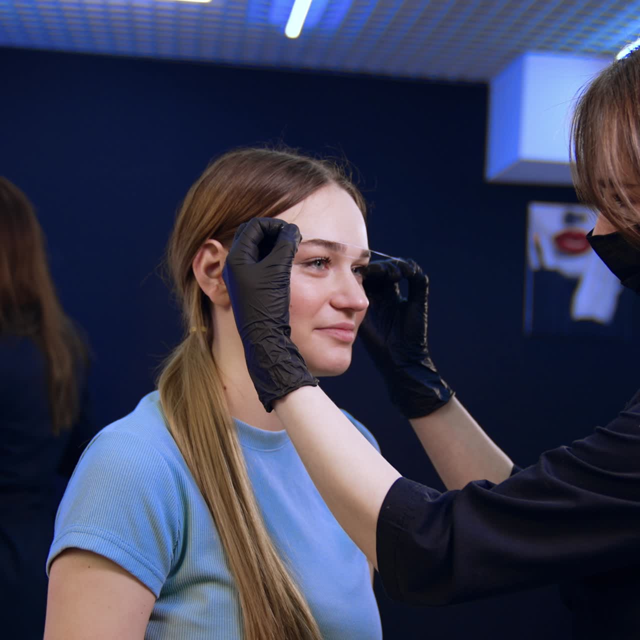 Brunette long-haired cosmetologist draws white lines for eyebrows with the help of a thread. Brow masters work in the salon
