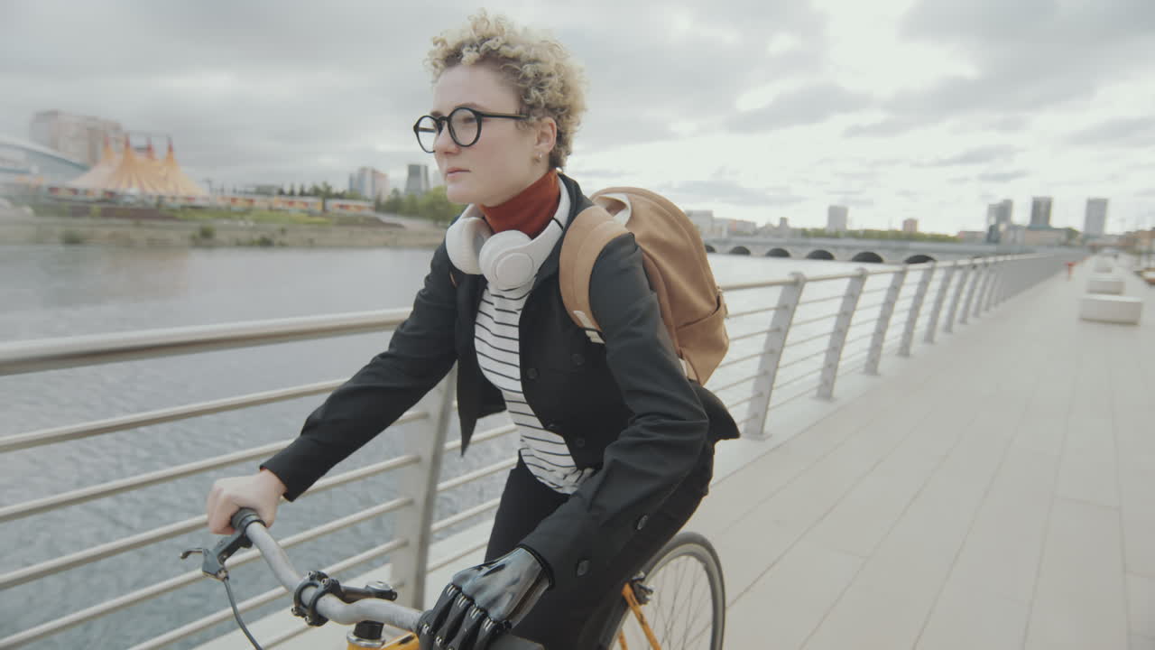 Girl with Prosthetic Arm Cycling on Urban Embankment