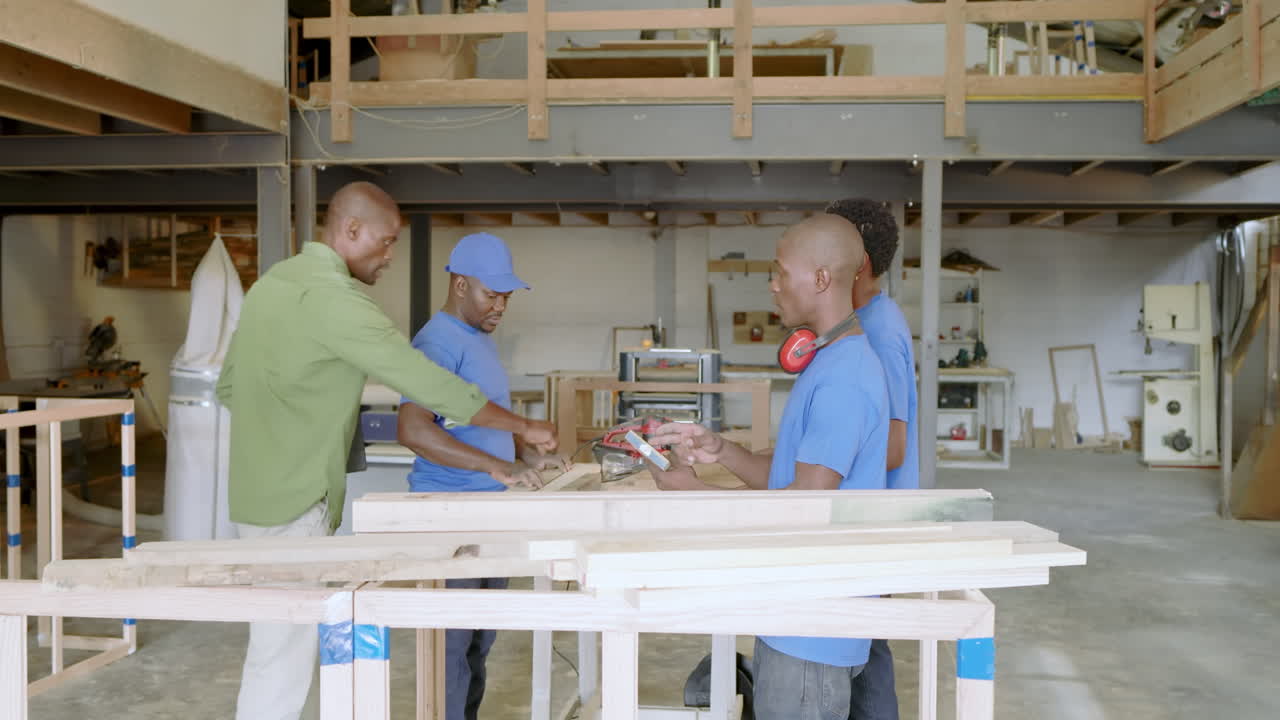 African American team entering workshop and sorting wood planks under supervisor guiding via tablet