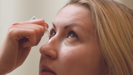 pretty young woman squeezing artificial tears into eyes with an eye dropper