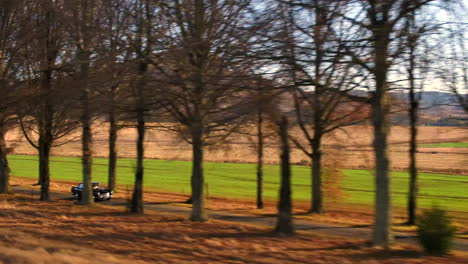 tracking drone shot alongside a black vintage austin westminster car driving through a road with trees on either side