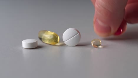 different color vitamin pills and capsules on table, person take red iron pill