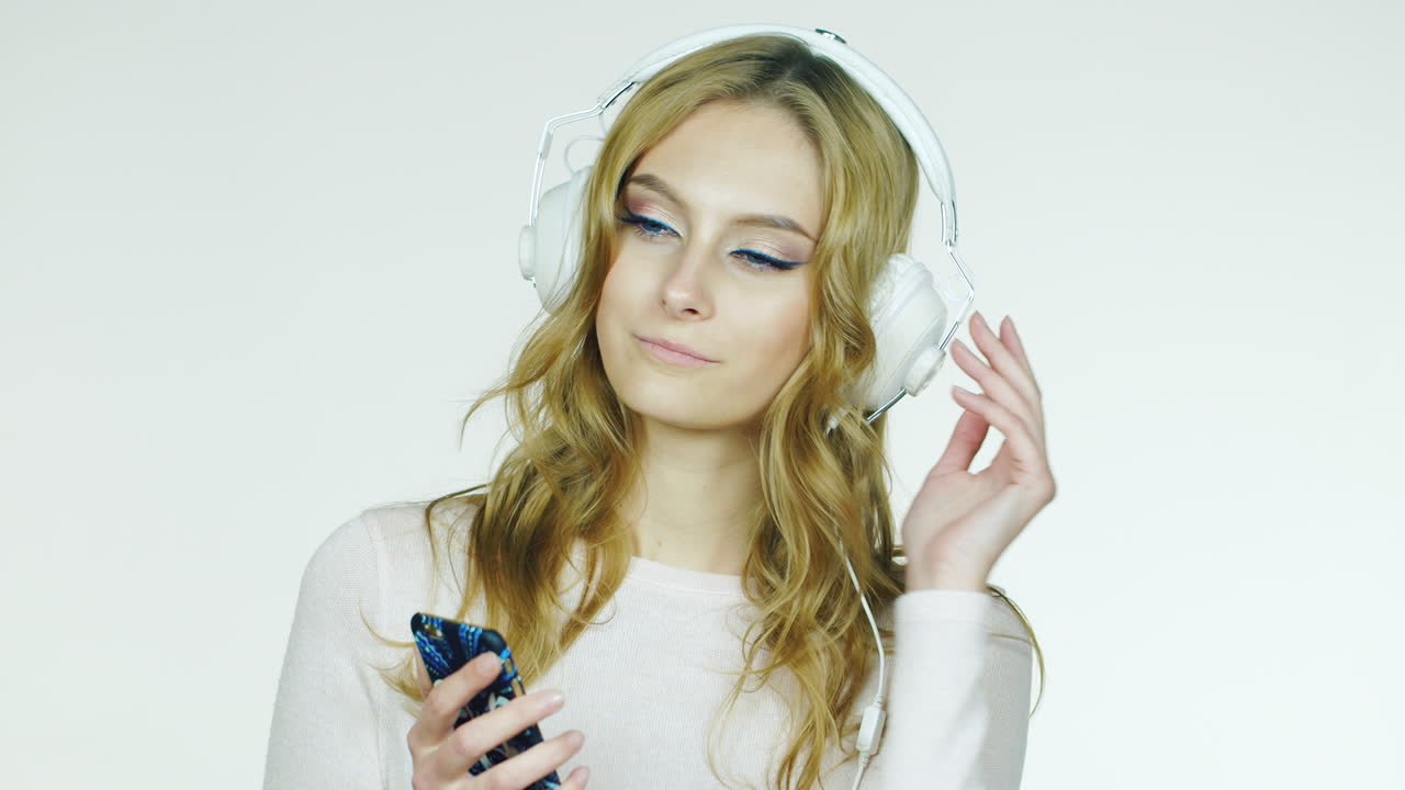Donna attraente che ascolta musica romantica con le cuffie su sfondo bianco. Video HD.