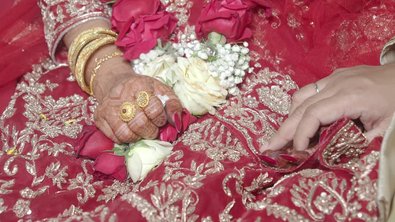 Nærbillede af brudeparrets hænder med blomster og traditionel beklædning ved en bryllupsceremoni