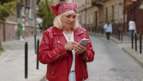 Senior woman use smartphone typing text messages browsing internet finishing work looking at camera