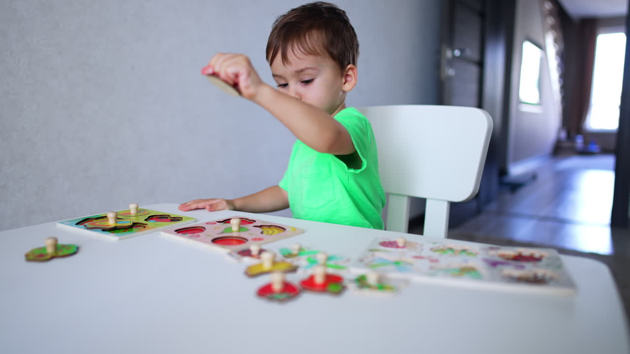 Focused baby boy playing with puzzles at desk. Cute kid learning fruit through a game.