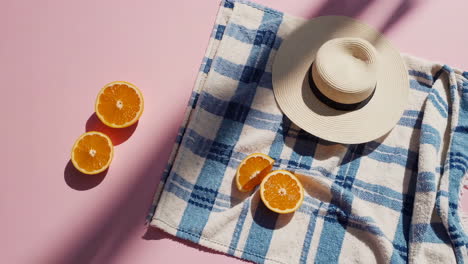 summer essentials: oranges, beach towel, and sun hat on pink background