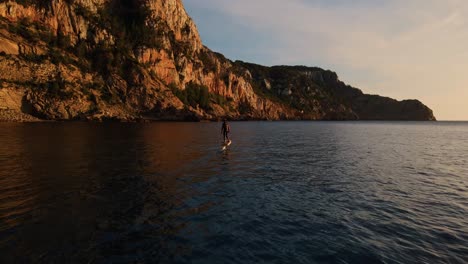 Drone-shot-following-an-electric-surfboard-along-the-steep-cliffs-of-Ibiza,-Spain