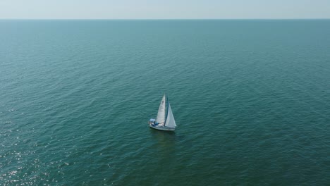 Luftaufnahme-Eines-Weißen-Segelboots-Im-Ruhigen-Meeresmeer,-Weiße-Segelyacht-Mitten-Im-Grenzenlosen-Meer,-Sonniger-Sommertag,-Weite-Umlaufende-Aufnahme