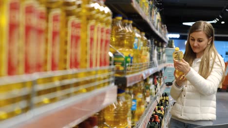 a young woman who picks up a bottle of olive oil in the supermarket. buying vegetable oil. slow motion