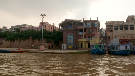 Cinematic-Varanasi-India-Ganges-River-birds-flying-chow-on-cruise-canal-boat-Northern-State-Ancient-Holy-city-Ghat-Pradesh-Province-landscape-gray-cloudy-Holy-muddy-brown-afternoon-sunset-follow-left