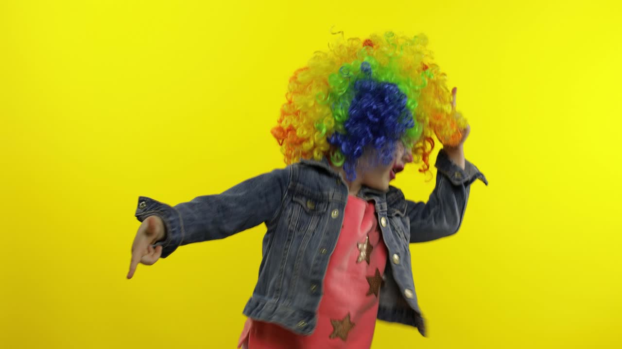 una niña payasa con una peluca colorida haciendo caras tontas. divirtiéndose, sonriendo, bailando. halloween