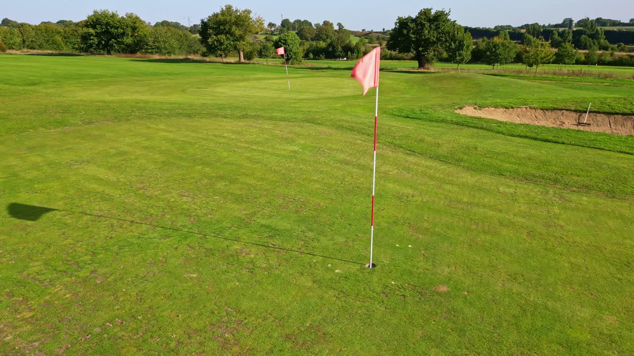 Golfbane med rød flaggstang stående på jevnt puttingområde, flyfoto som sporer rett medium