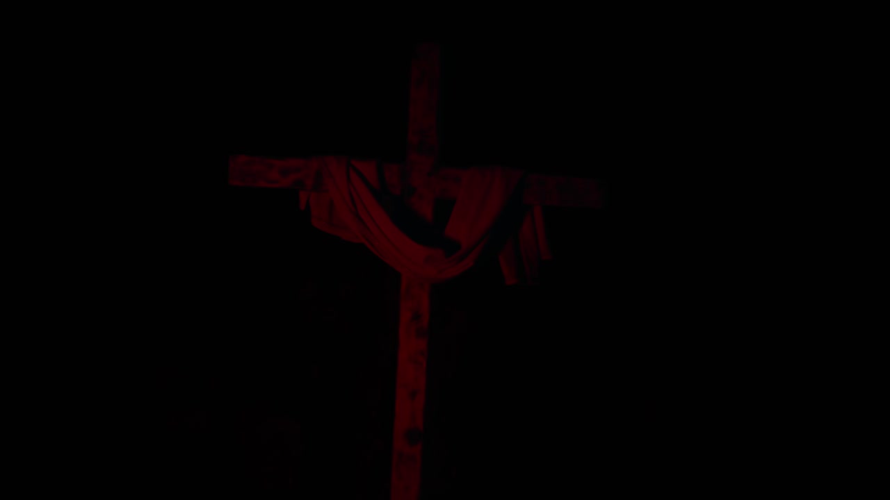 Dark scene of wooden cross with draped cloth as red light fades in and out