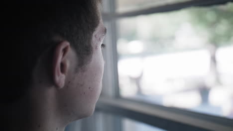 sad, depressed, unhappy young man, teenage boy looking out window in cinematic slow motion