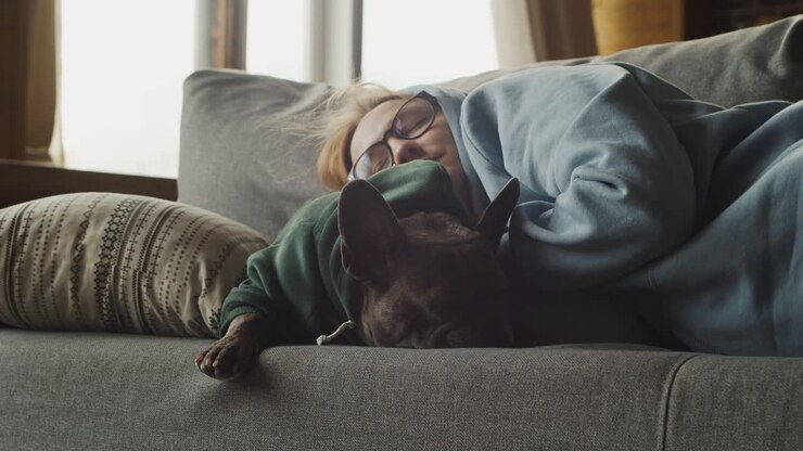 Mujer pelirroja durmiendo con su perro bulldog en el sofá del salón de casa.