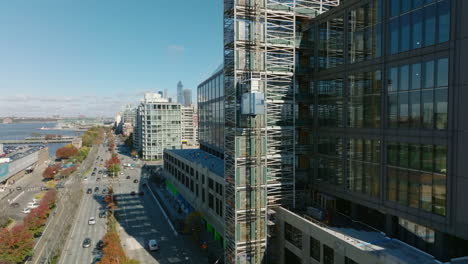 Rising-shot-tracking-of-construction-lift-moving-up-along-building-wall.--Wide-multilane-waterfront-road.-Manhattan,-New-York-City,-USA