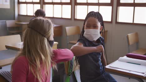 two girls wearing face masks greeting each other by touching elbows at school