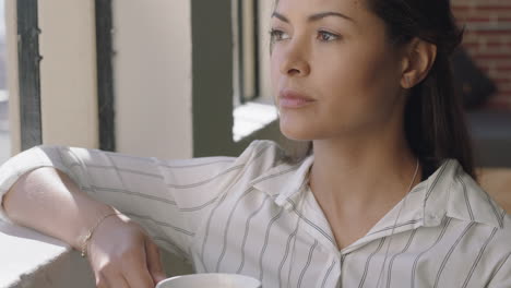 beautiful hispanic woman drinking coffee at home enjoying relaxed morning looking out window thinking contemplative