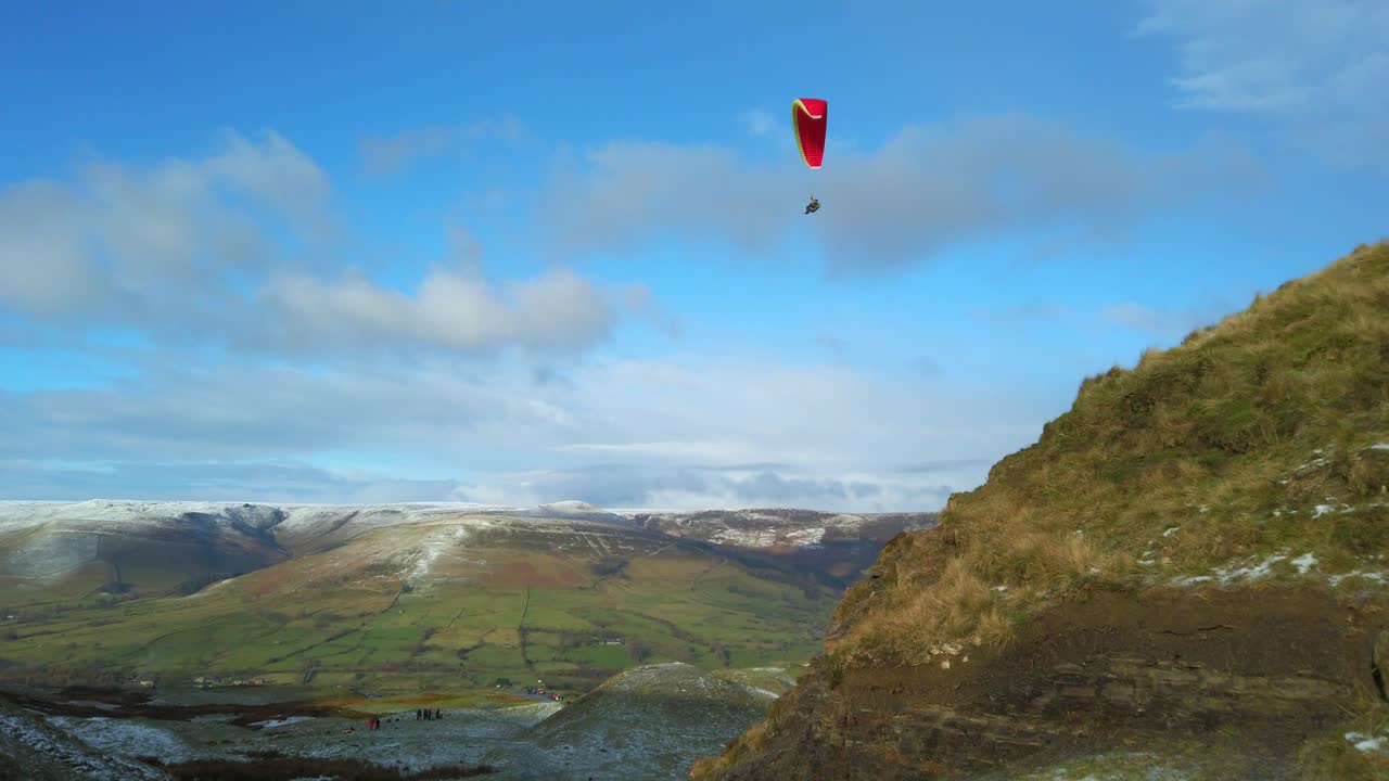 Aerial view paraglider flys between green fields valley with snow on horizon