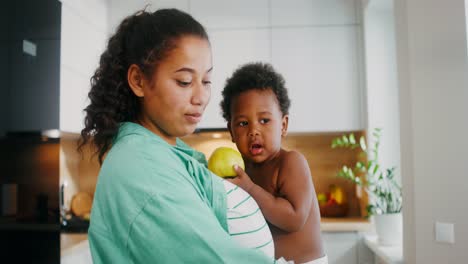 mother feeding baby an apple in the kitchen
