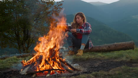 camp woman relax mountains. close up beautiful girl sit enjoy bonfire on nature.